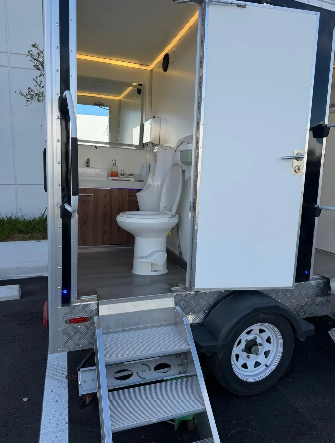 Restroom trailer stall with a flushing toilet, wood vanity and LED lighting
