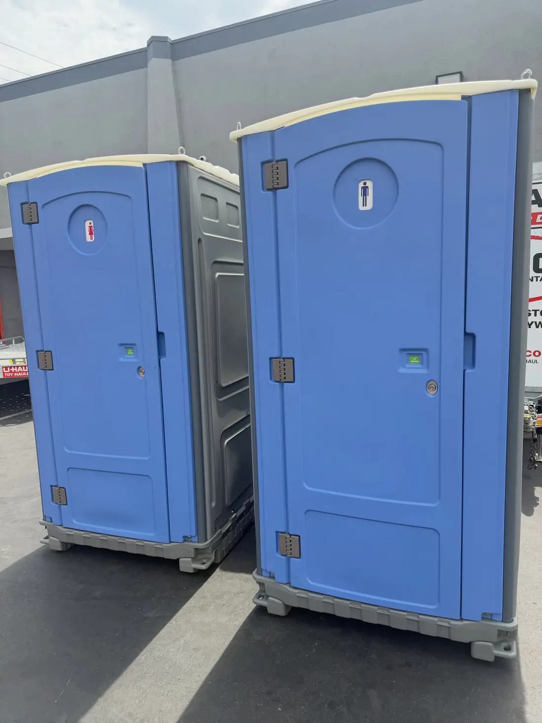 Two blue standard porta potties on pavement