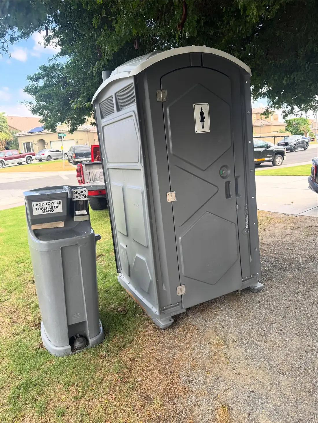 Gray standard porta potty with a separate hand-washing station set on a grass lawn